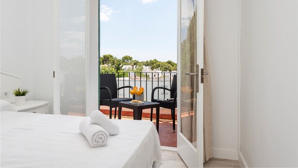 A hotel room with a bed, a small table with a plant, and a balcony with chairs and a table. - Hostal Talamanca (Santanyi)