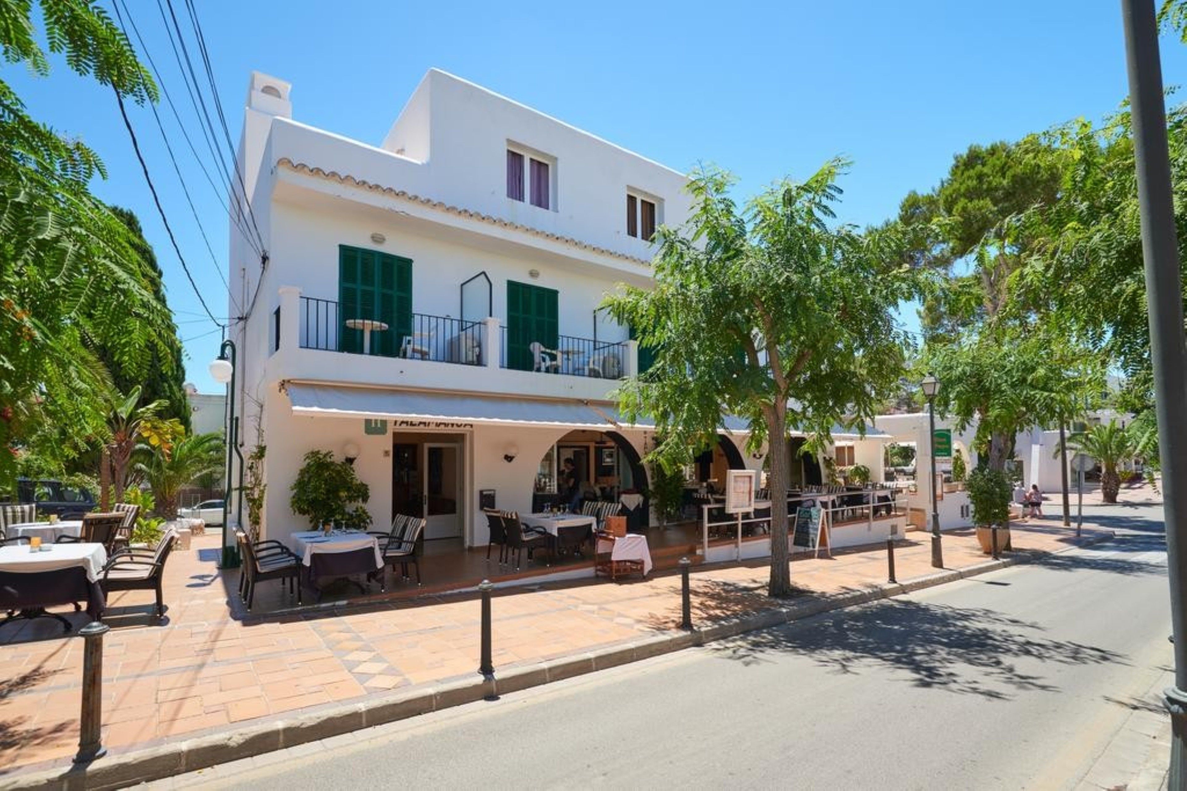 Un edificio de dos plantas con una cafetería en la planta baja, mesas al aire libre y un balcón.