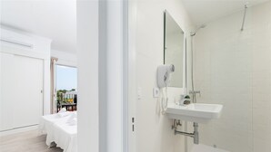 A hotel room with a bed, a bathroom with a sink and shower, and a view of the outdoors. - Hostal Talamanca (Santanyi)