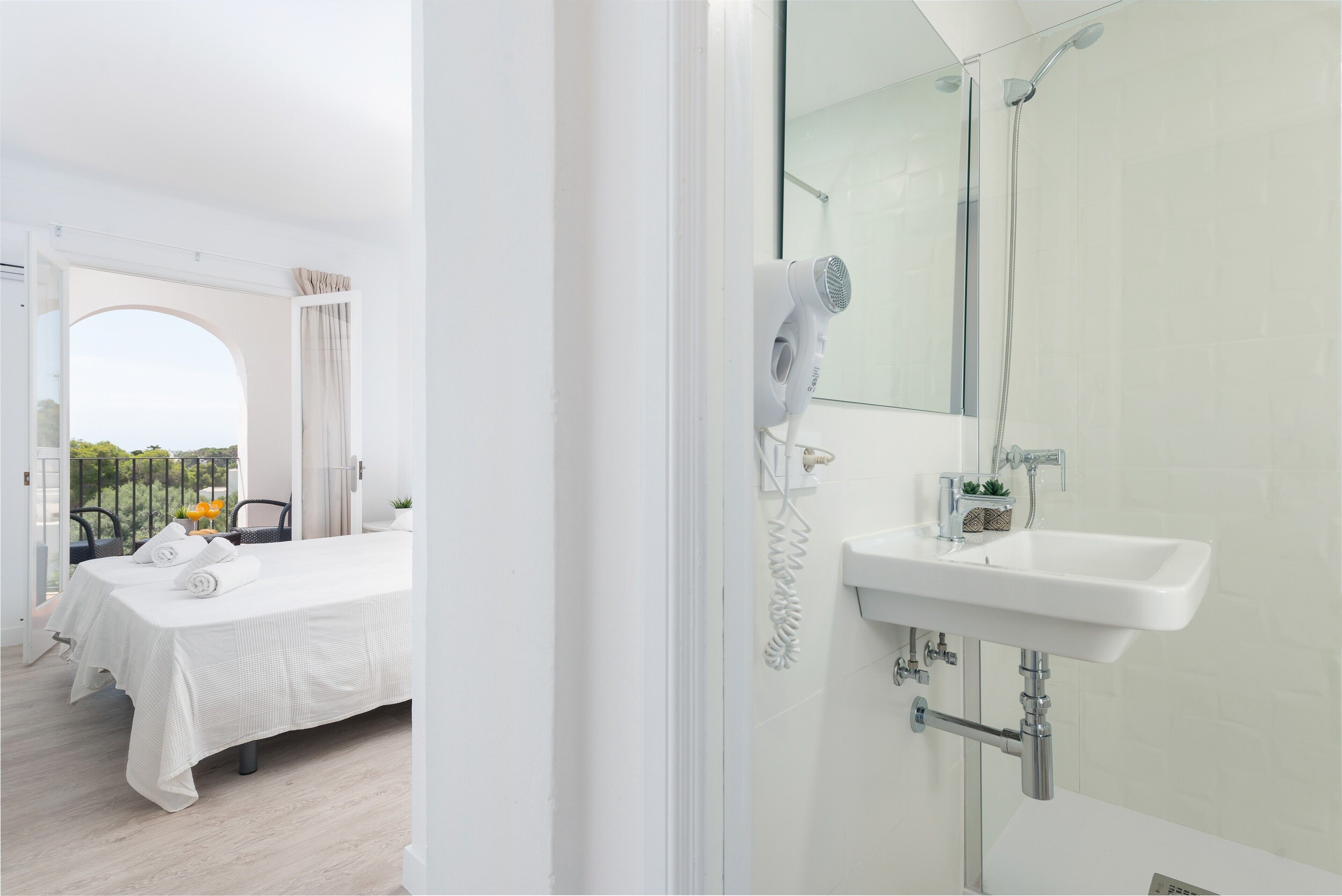 Una habitación de hotel con cama, baño con lavamanos y espejo, y vistas al exterior.