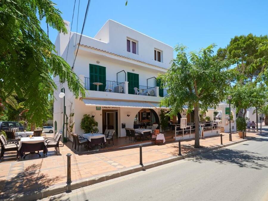 Un edificio de dos pisos con una cafetería en la planta baja, mesas al aire libre y un balcón con barandas verdes.
