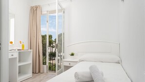 A bedroom with a bed, a bedside table, a nightstand, a mirror, a window with curtains, and a balcony with a view. - Hostal Talamanca (Santanyi)