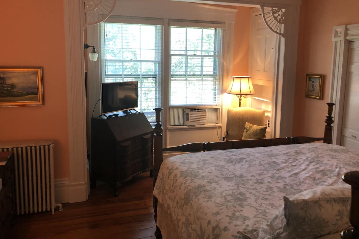 Un dormitorio con cama, cómoda, televisor, lámpara y ventana con persianas.
