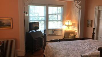 Een slaapkamer met een bed, een dressoir, een televisie, een lamp en een raam met jaloezieën.
