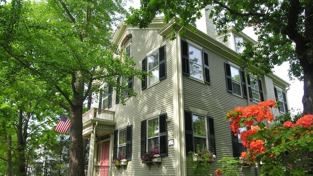A two-story house with a front porch, a stone wall, and a well-maintained garden. - Delano Homestead Bed & Breakfast (Fairhaven)