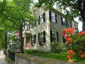 A two-story house with a front porch, a stone wall, and a well-maintained garden.