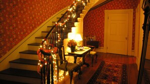 A staircase with a railing decorated with lights, a table with a lamp, and a chair. - Delano Homestead Bed & Breakfast (Fairhaven)