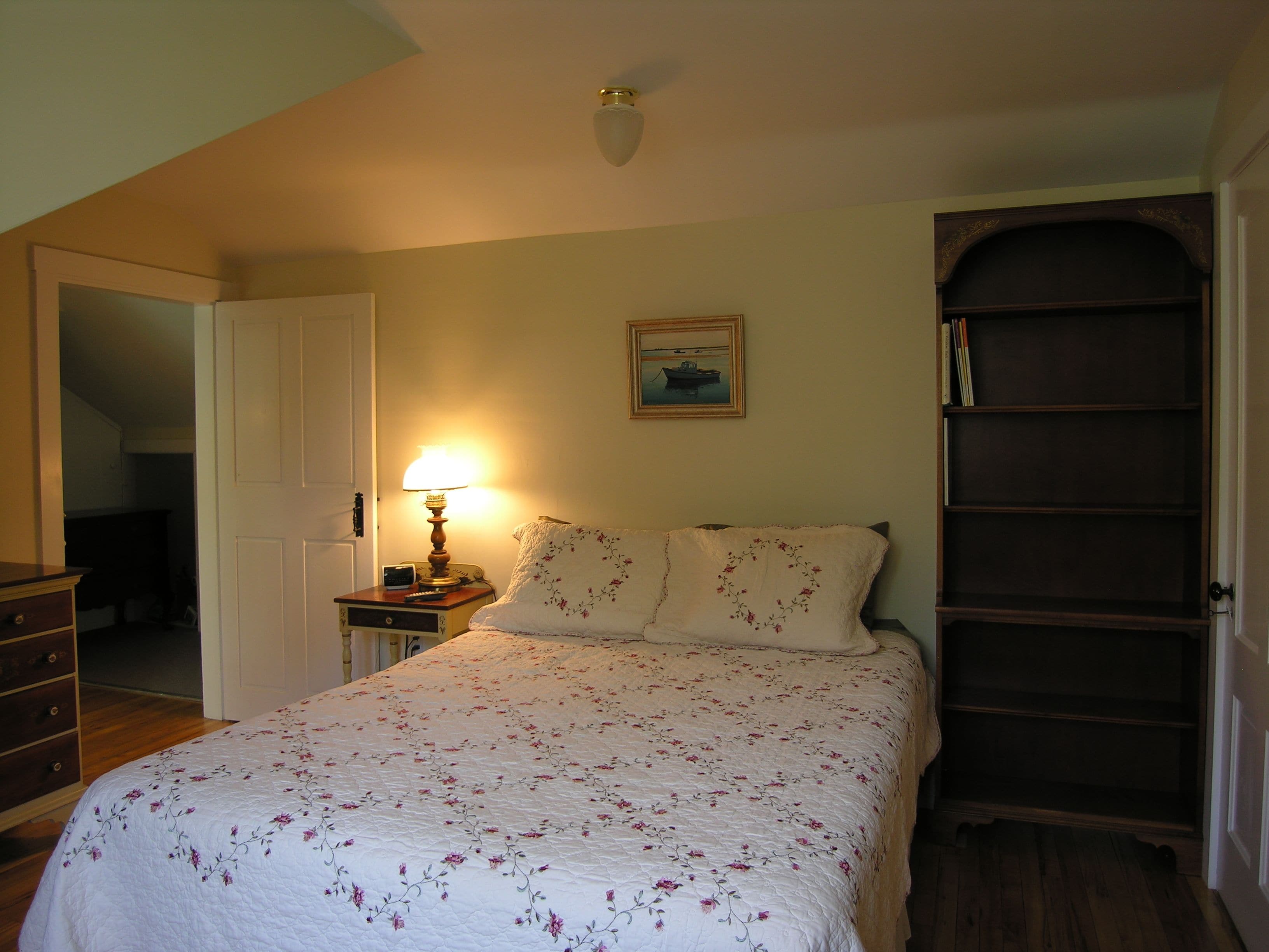 Une chambre à coucher avec un lit, une table de chevet avec une lampe, un tableau au mur et une armoire en bois.
