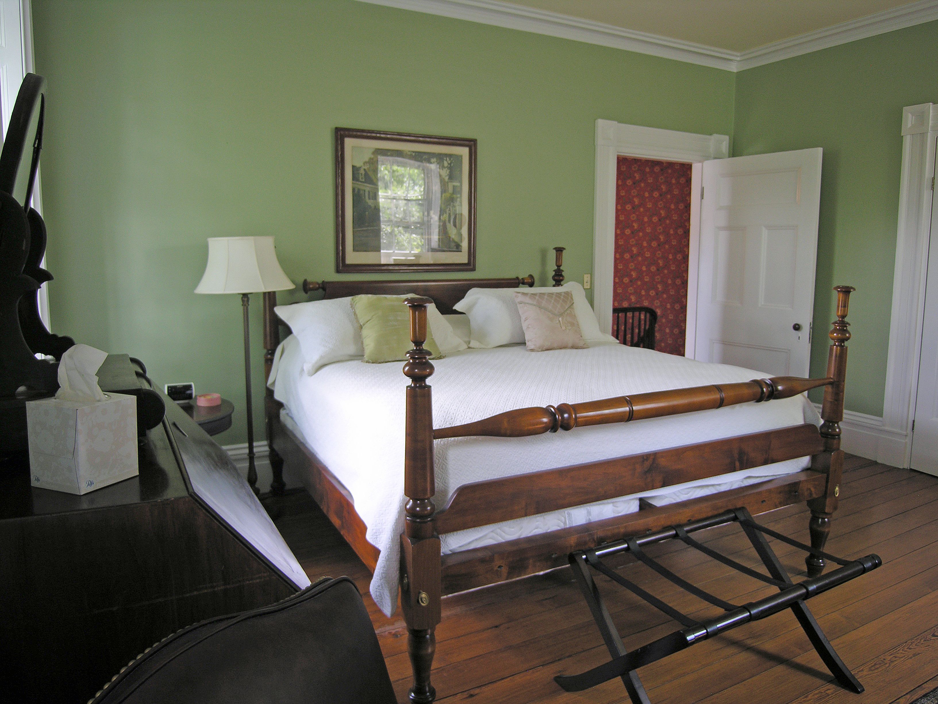 A bedroom with a four-poster bed, a nightstand, a chair, and a door with a floral curtain.