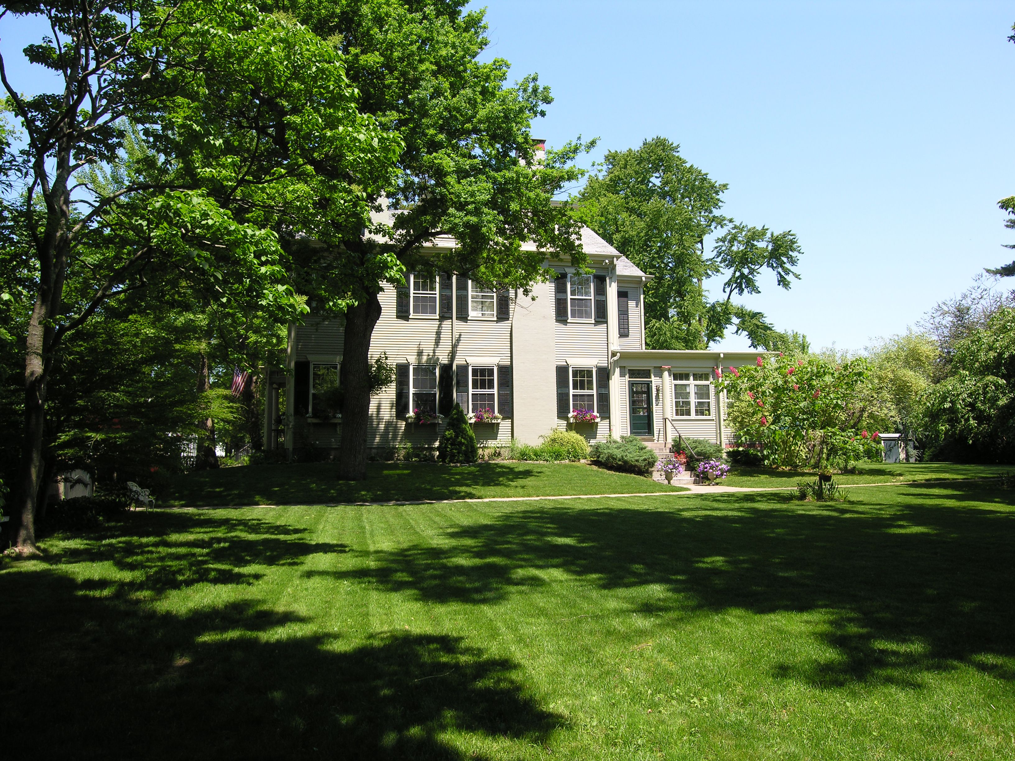 A two-story house with a well-maintained lawn and a large tree in the foreground.