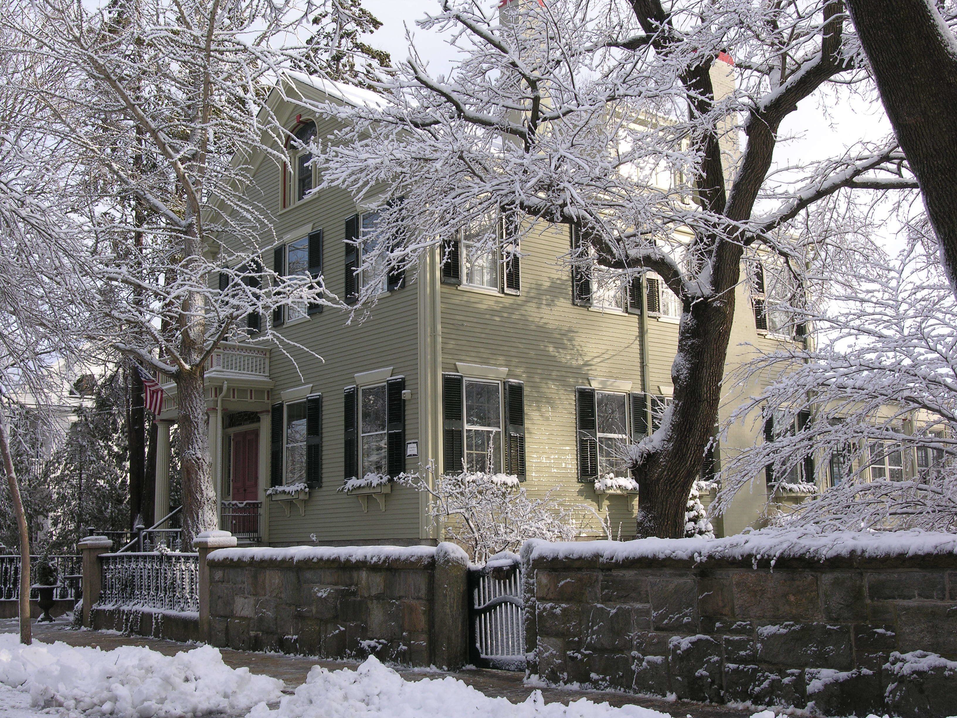 A two-story building with a stone wall in front, surrounded by snow-covered trees.