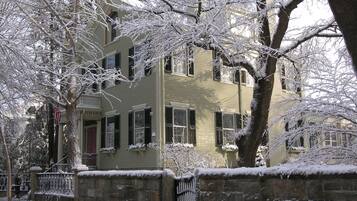 A two-story building with a stone wall in front, surrounded by snow-covered trees.