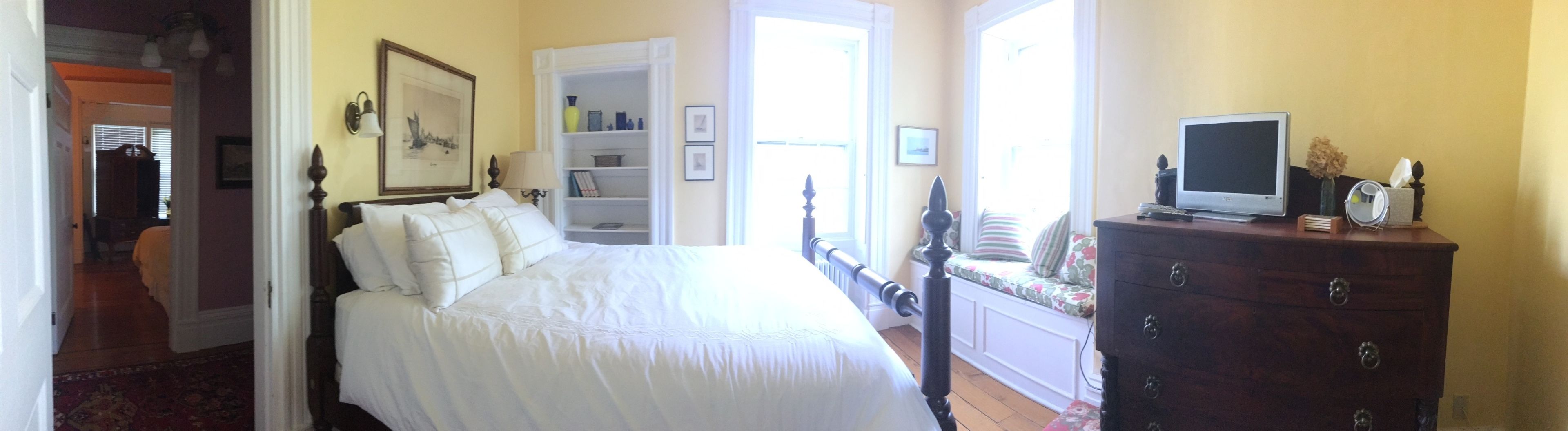 Quarto com cama, penteadeira, televisão e janela.