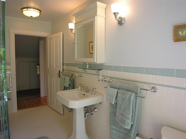 A bathroom with a white sink, a mirror, and a toilet. There are two wall-mounted lights and a towel rack with towels.