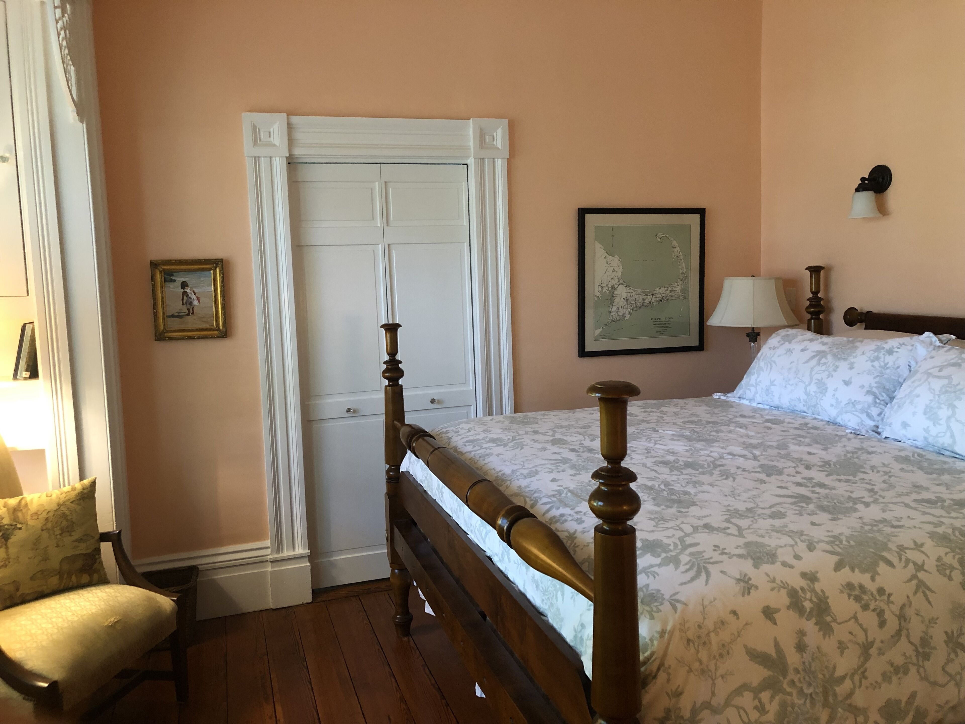 A bedroom with a wooden bed, a white door, a framed map on the wall, and a lamp.