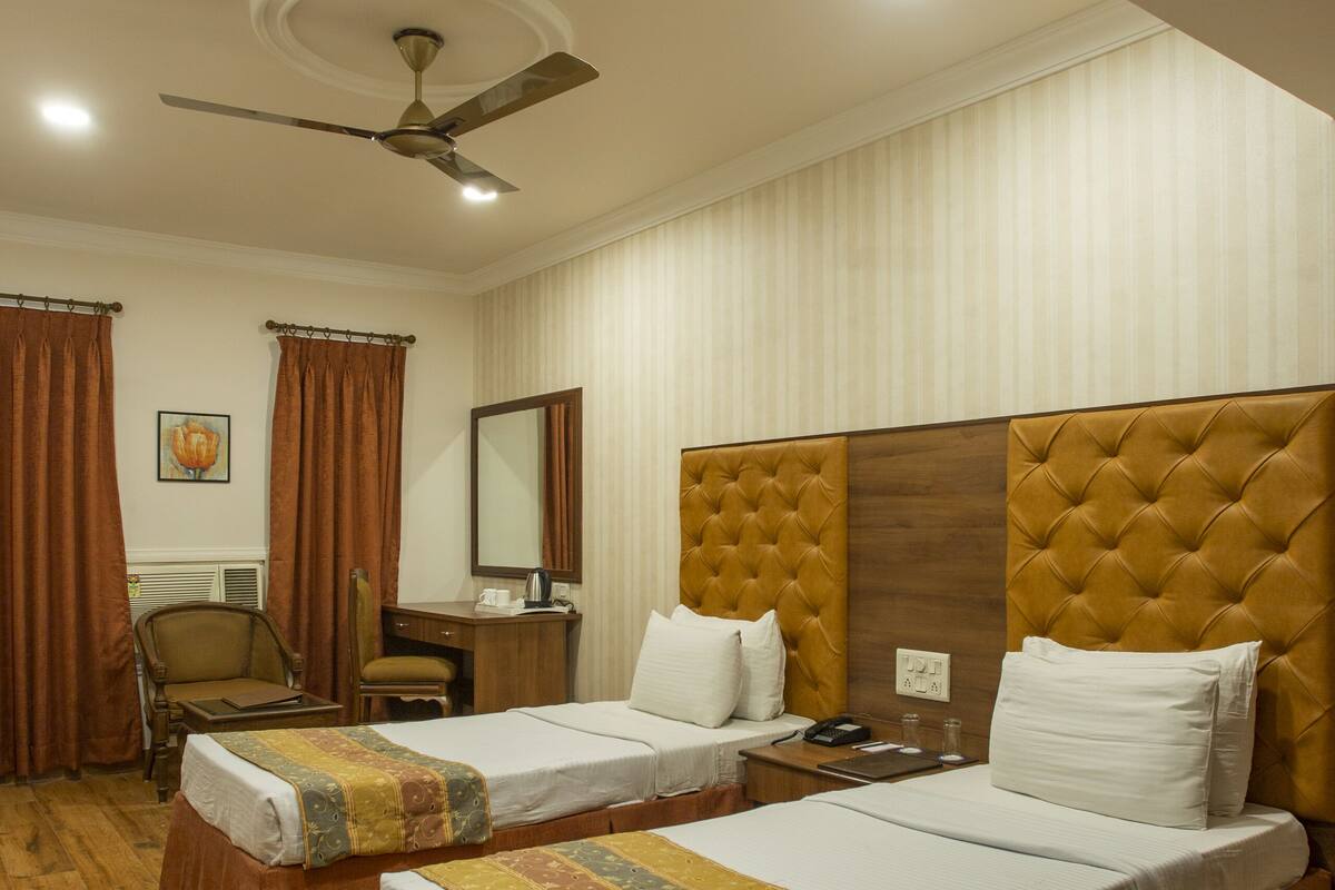 Une chambre d’hôtel avec deux lits, un bureau, une chaise et un ventilateur de plafond.