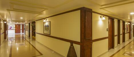 A hotel corridor with a polished floor, wooden paneling, and a large vase in the center.