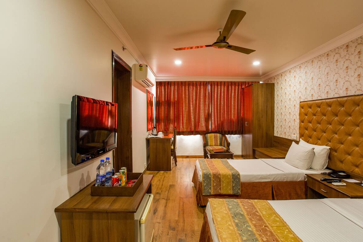 Une chambre d’hôtel avec deux lits, une télévision, un bureau et un ventilateur de plafond.