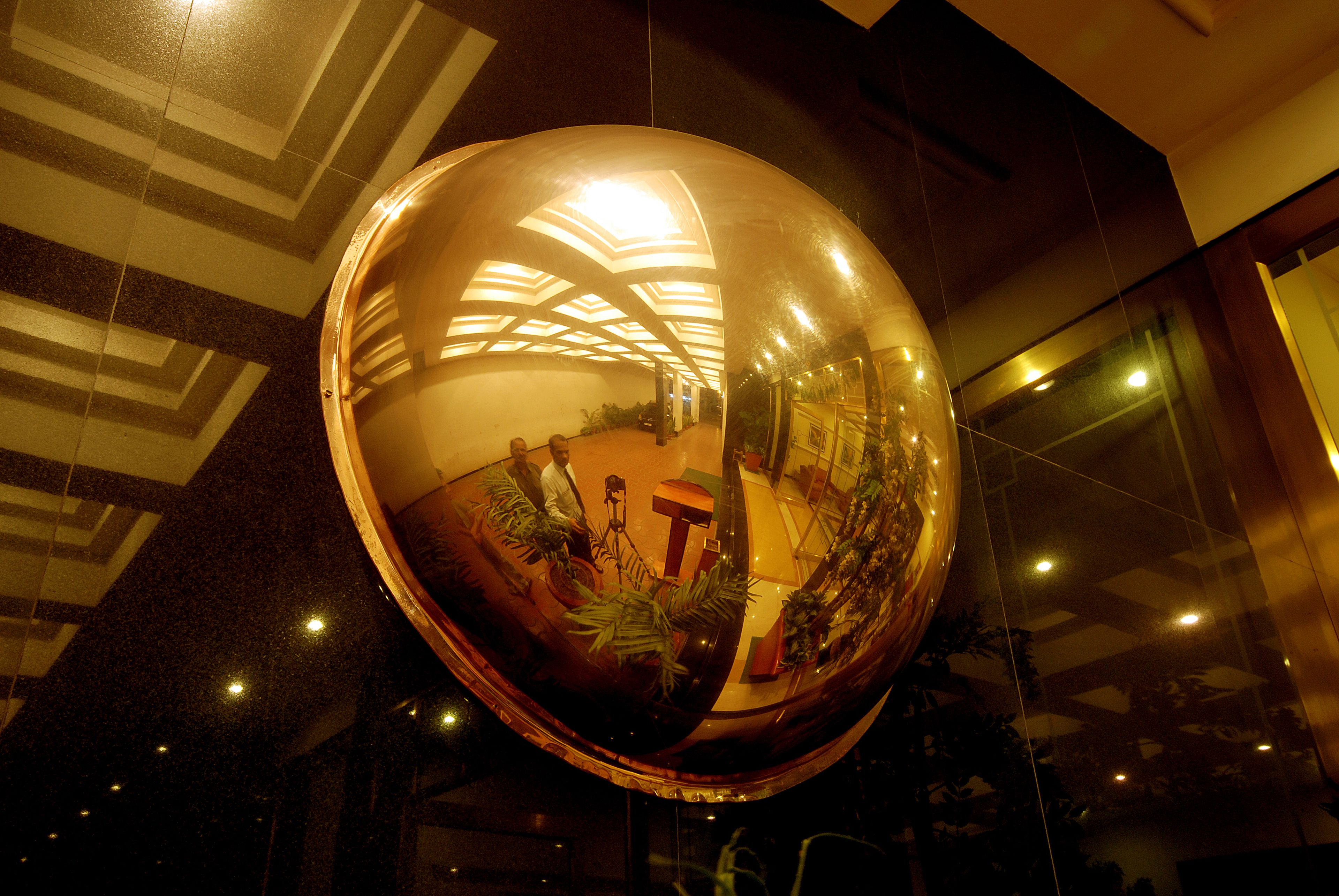 Un espejo esférico refleja un interior moderno con diseños geométricos en el techo y plantas en macetas.
