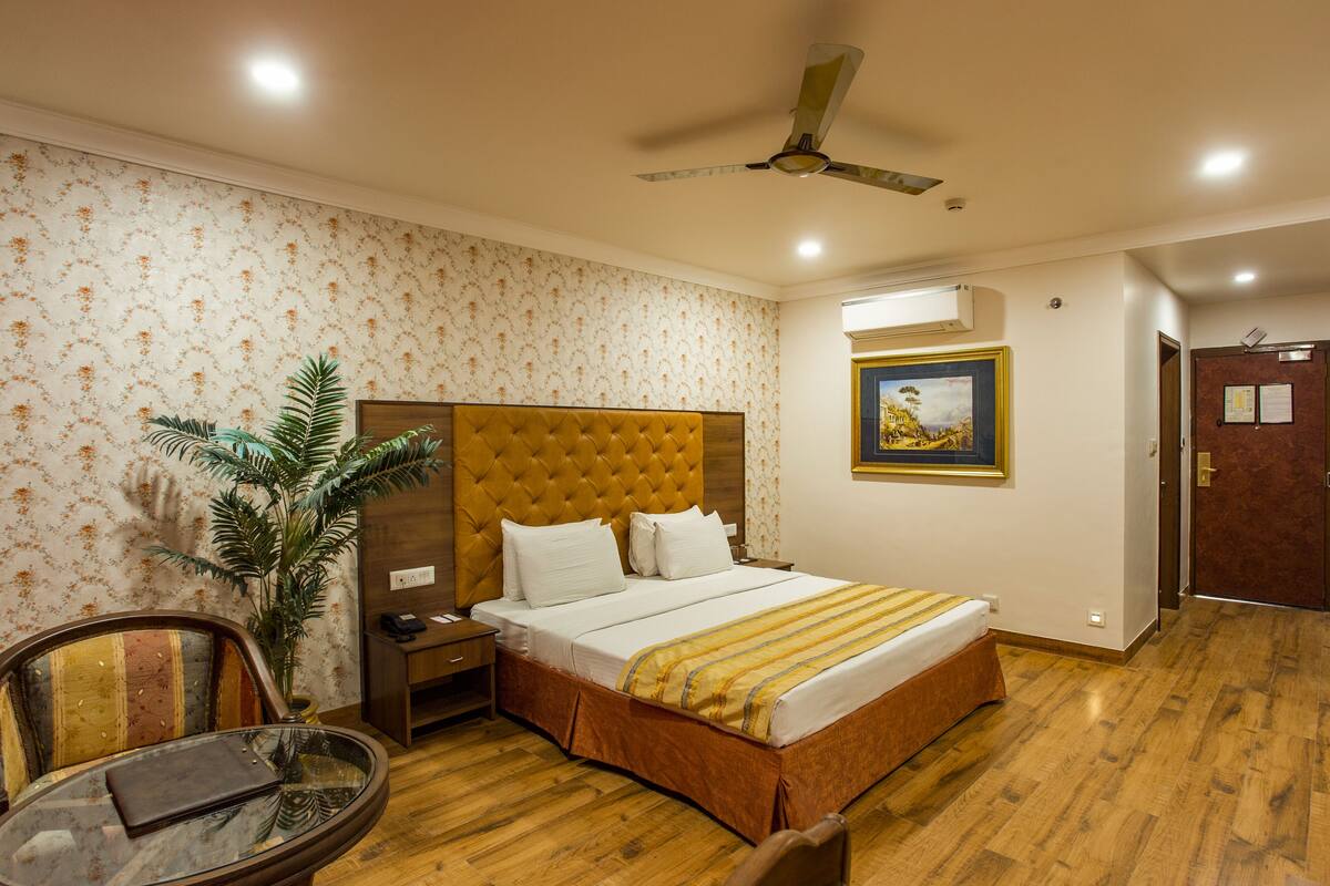 Une chambre d’hôtel avec un grand lit, une table de chevet, une chaise, une table, un ventilateur de plafond et un tableau au mur.