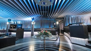 A modern lobby with a unique ceiling design, a reception desk, and a glass table with flowers. - Hotel Malligi (Hospet)