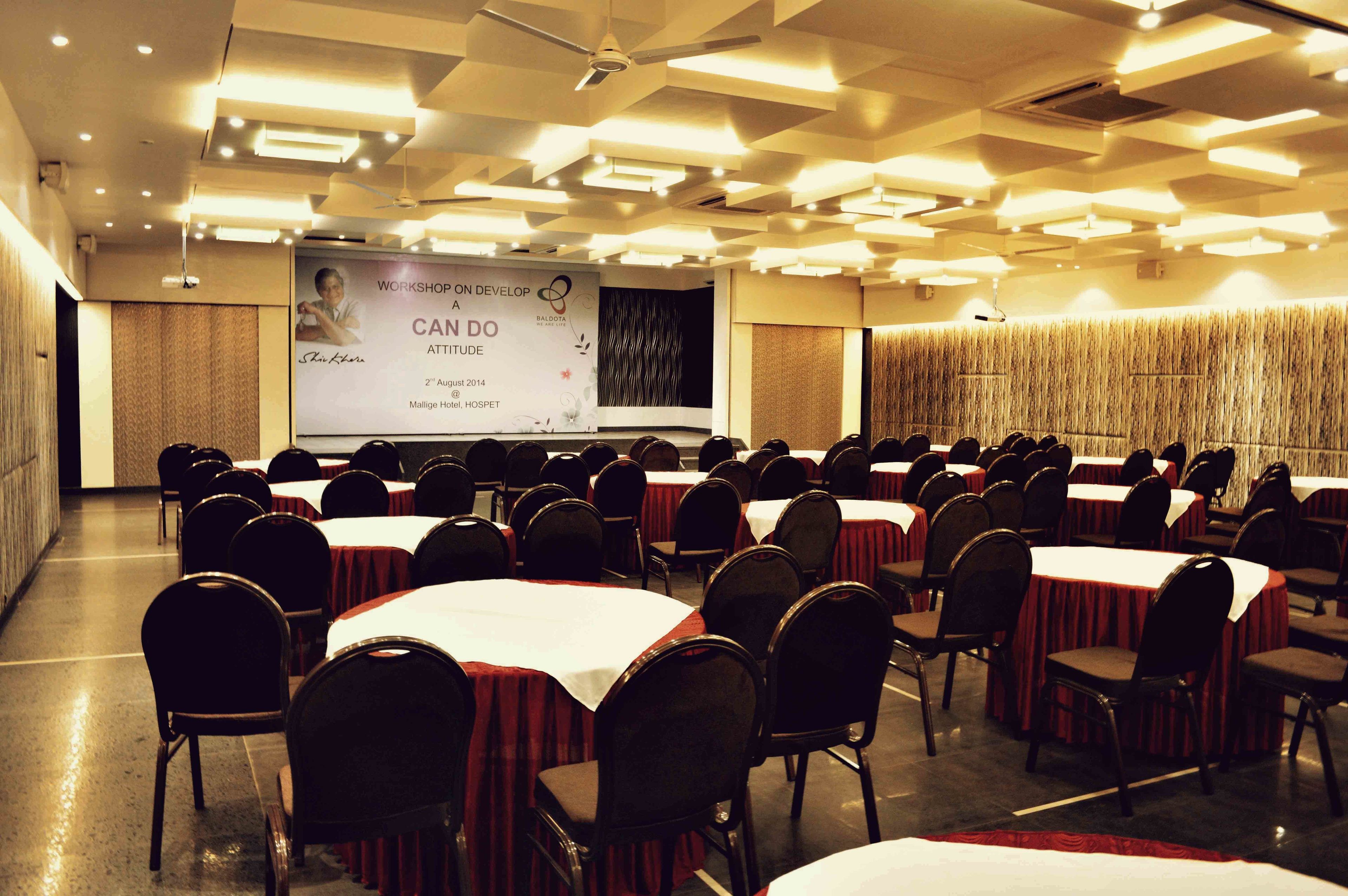 A conference room with rows of tables and chairs, a projection screen, and a banner on the wall.