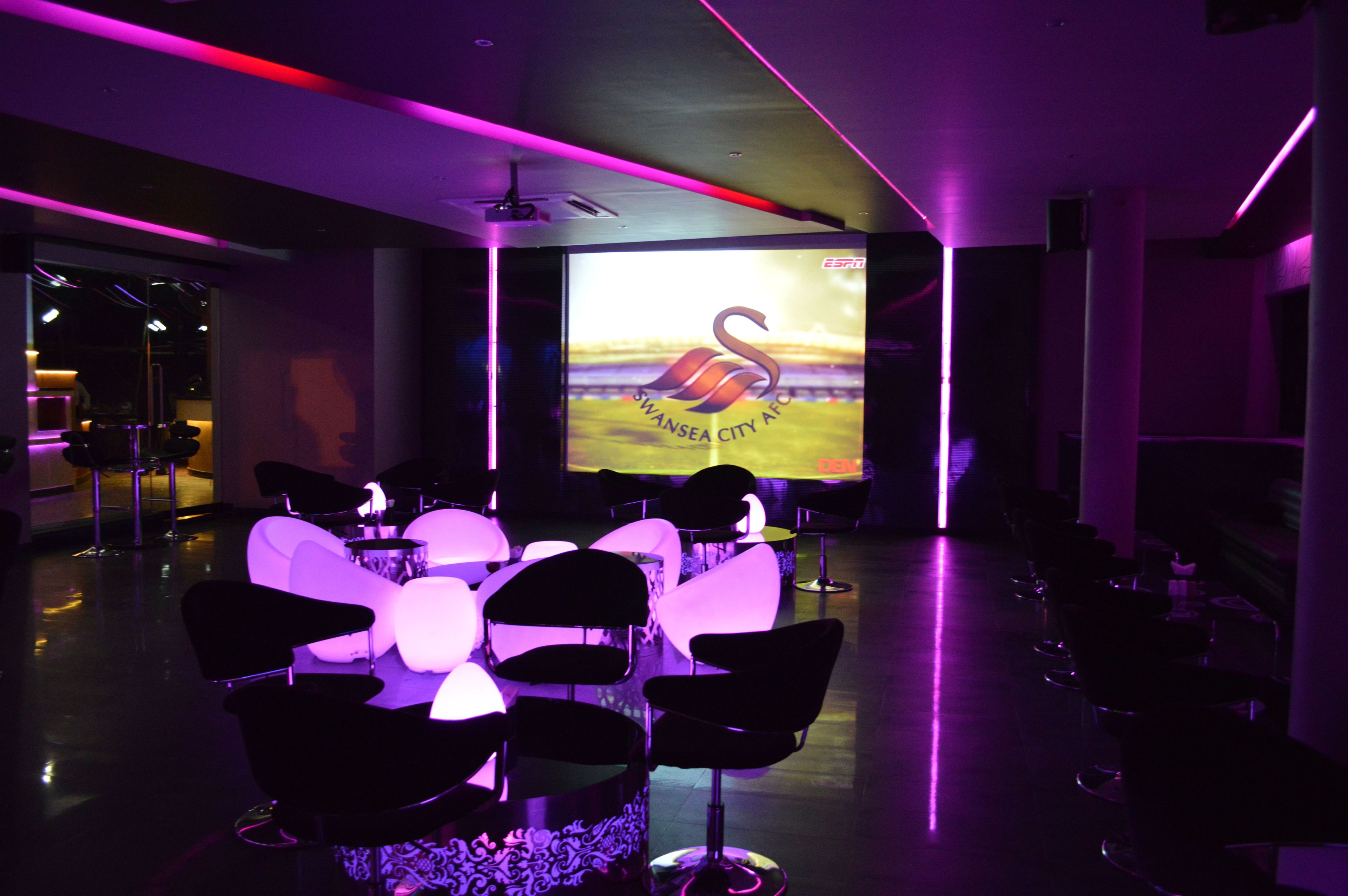 Un salón de conferencias con una pantalla grande mostrando el logotipo del Swansea City AFC, rodeado de sillas y mesas modernas.