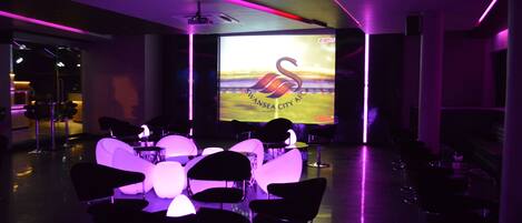 Un salón de conferencias con una pantalla grande mostrando el logotipo del Swansea City AFC, rodeado de sillas y mesas modernas.