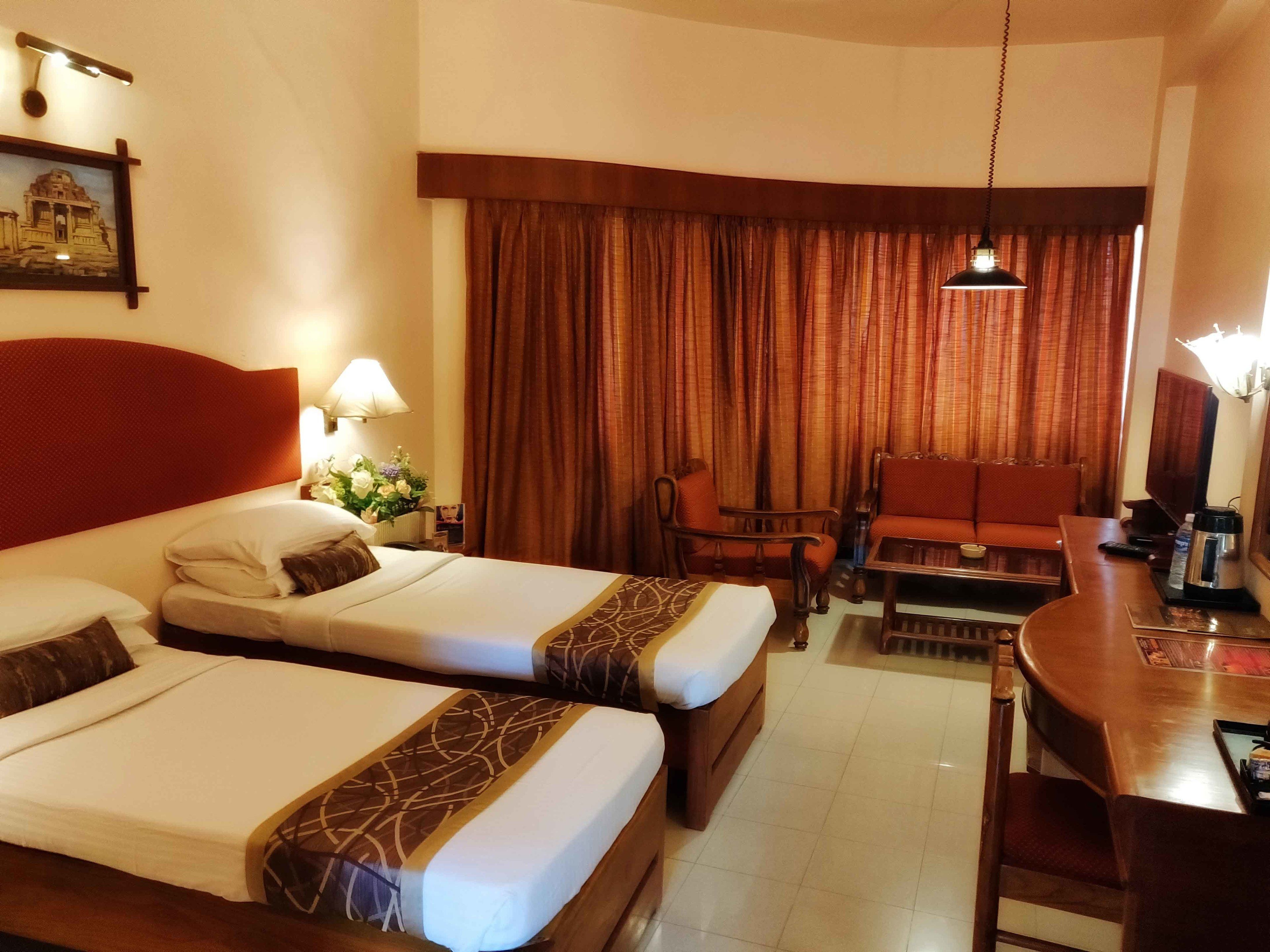 A hotel room with two beds, a sofa, a small table, a TV, and a coffee maker.