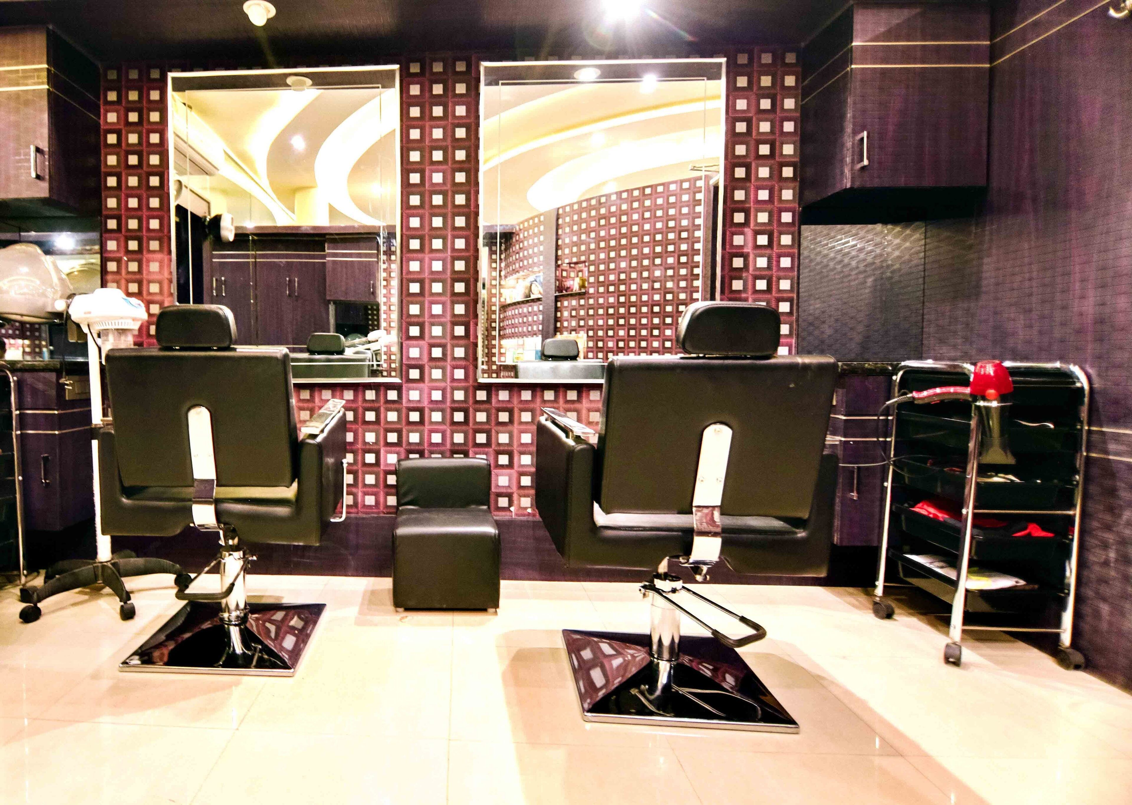 A salon with two black salon chairs, a mirror, and a shelf with red items.