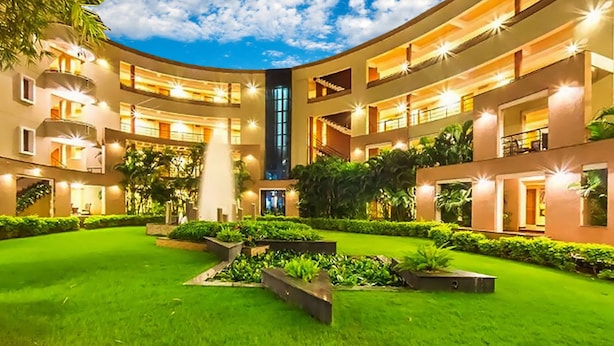 A multi-level hotel with a central courtyard, outdoor lighting, and lush greenery. - Hotel Malligi (Hospet)