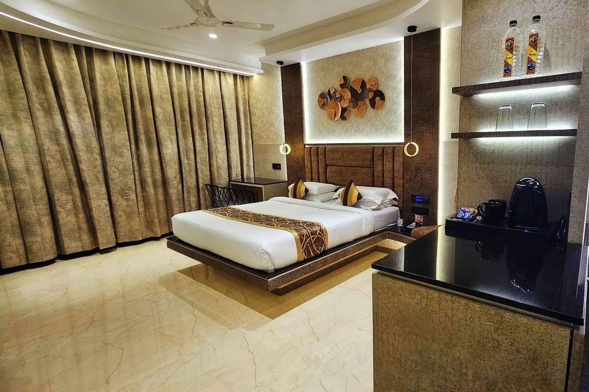 A modern hotel room with a large bed, a desk, a coffee maker, and a wall-mounted shelf with bottles.