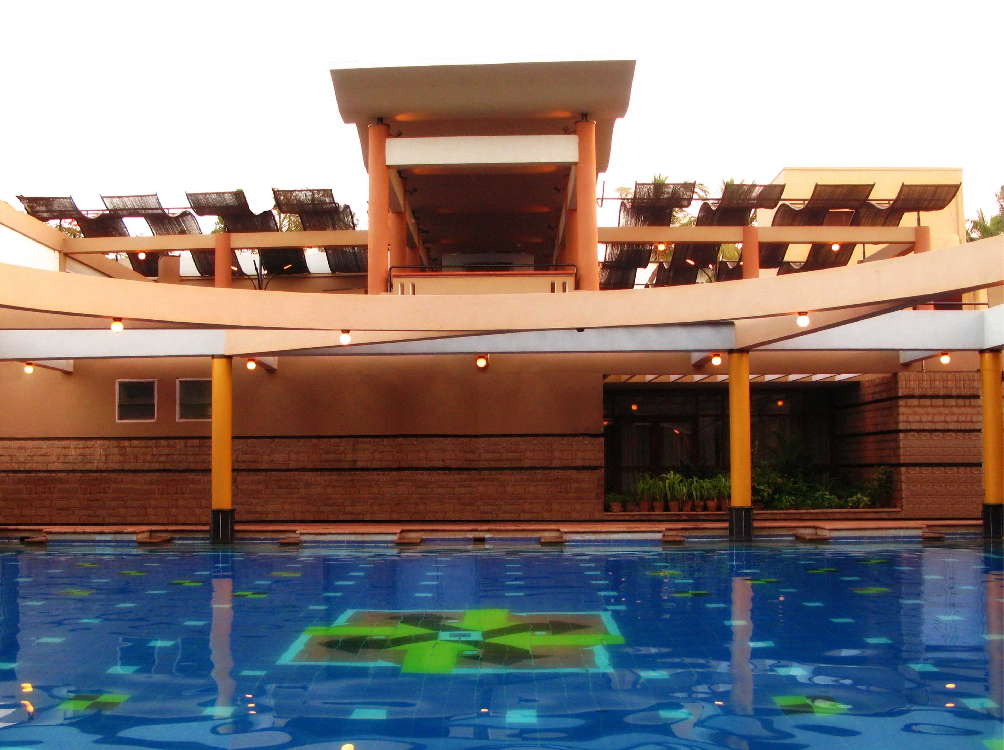 A swimming pool with a geometric pattern on the floor, surrounded by a covered area with seating and a brick wall.