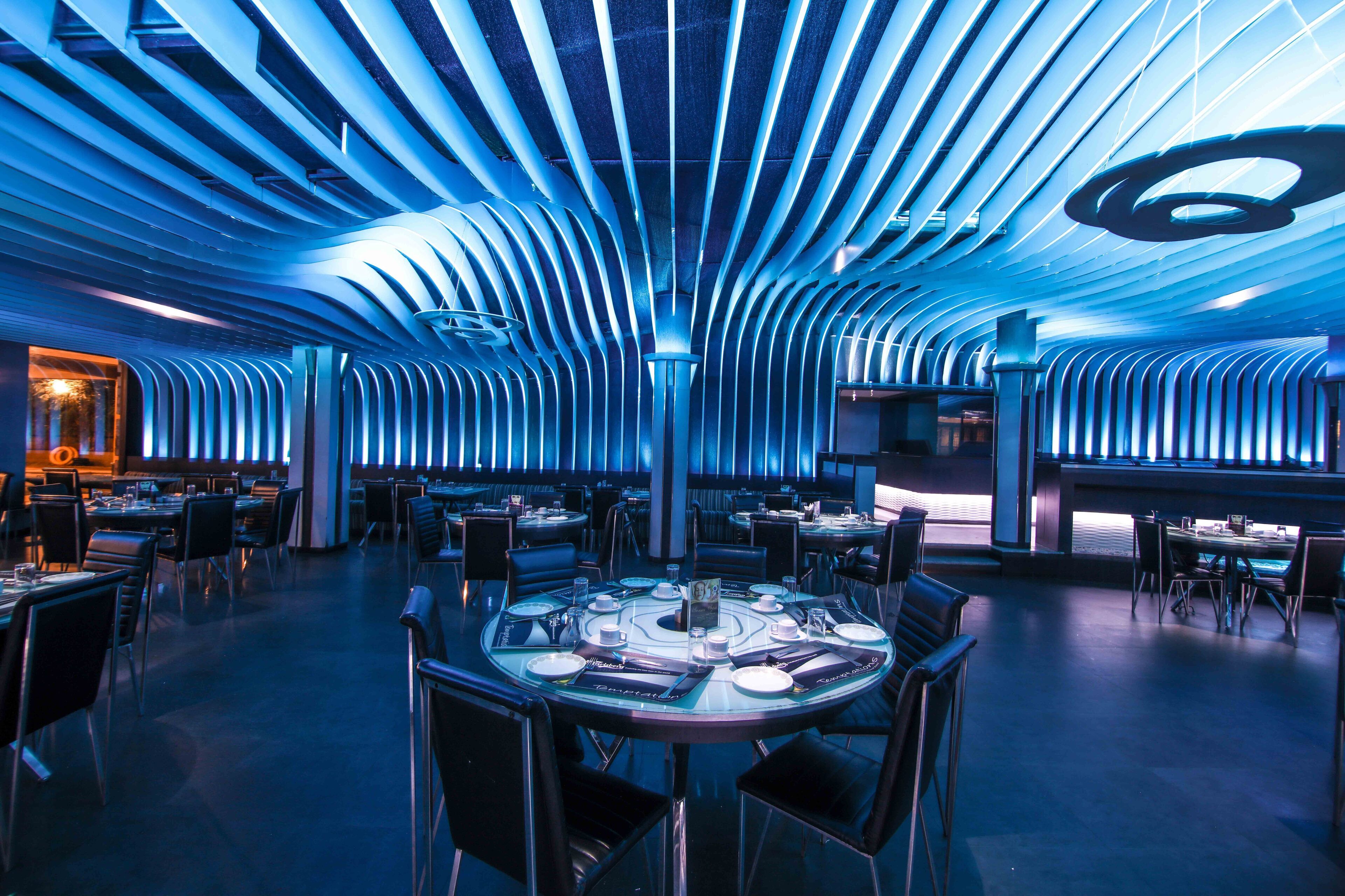 Um restaurante moderno com design de teto diferenciado e uma mesa central rodeada por cadeiras.