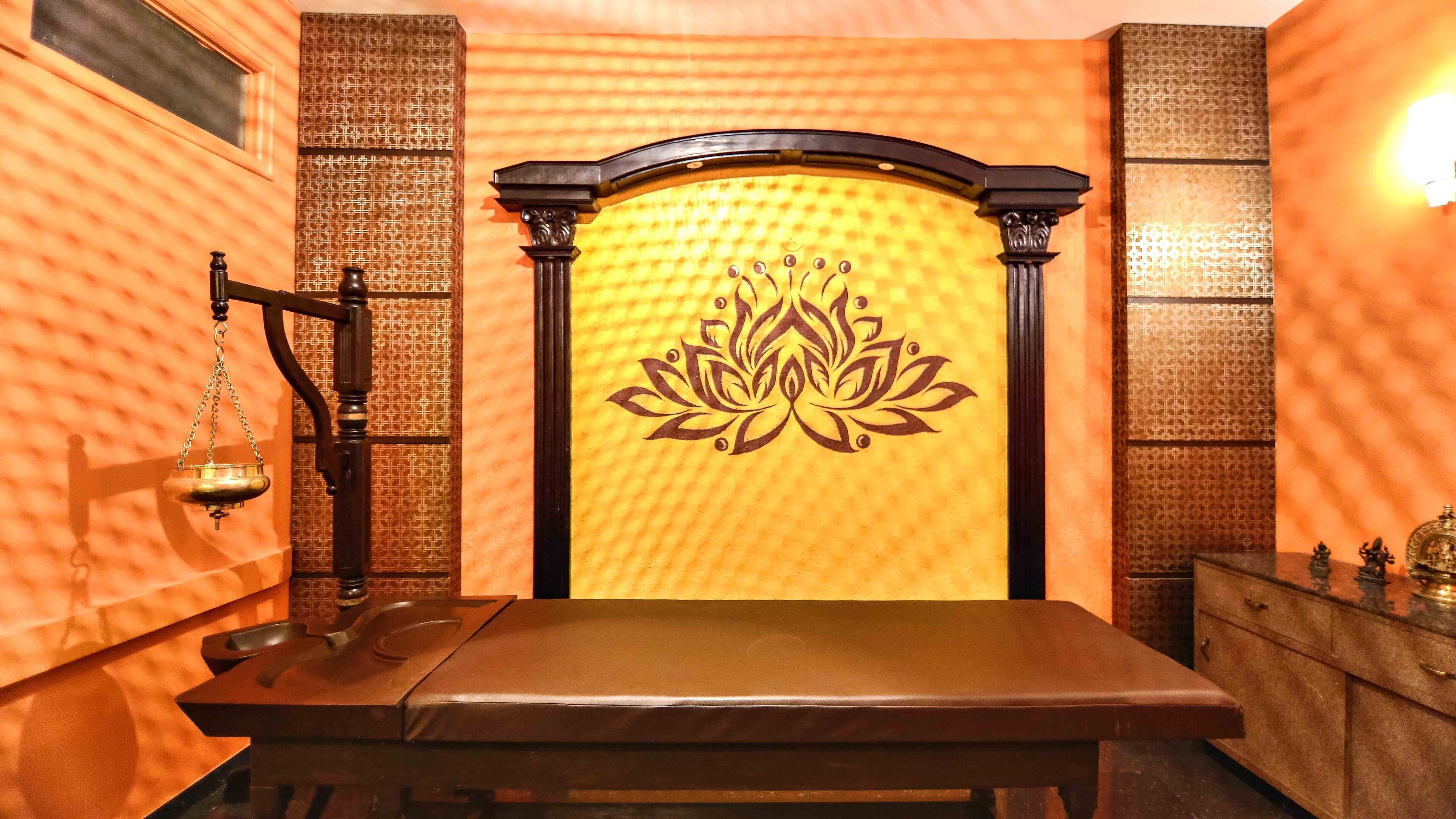 A room with a bed, a massage table, and a decorative wall with a lotus design.