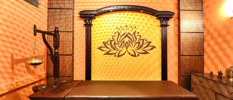 A room with a bed, a massage table, and a decorative wall with a lotus design.