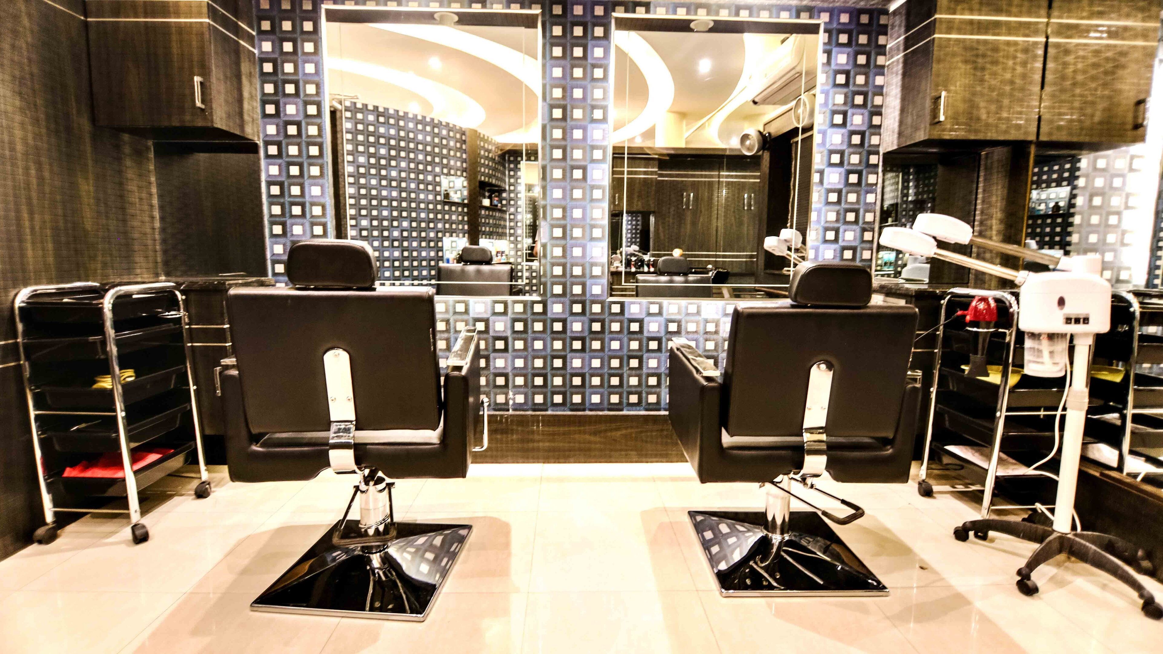 A modern salon with two black salon chairs, a mirror, and a sink.