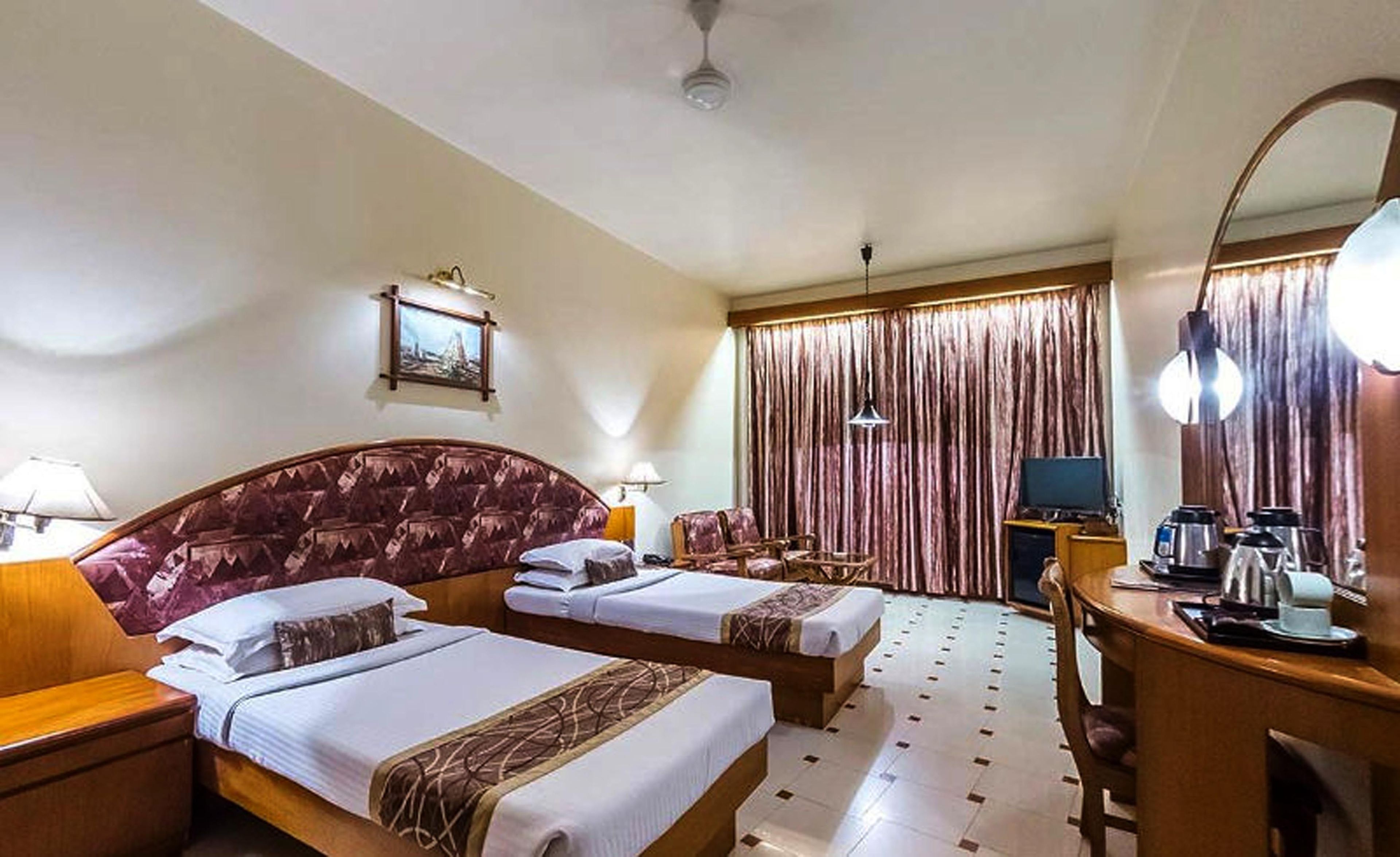A hotel room with two beds, a desk with a mirror, a television, and a coffee machine.