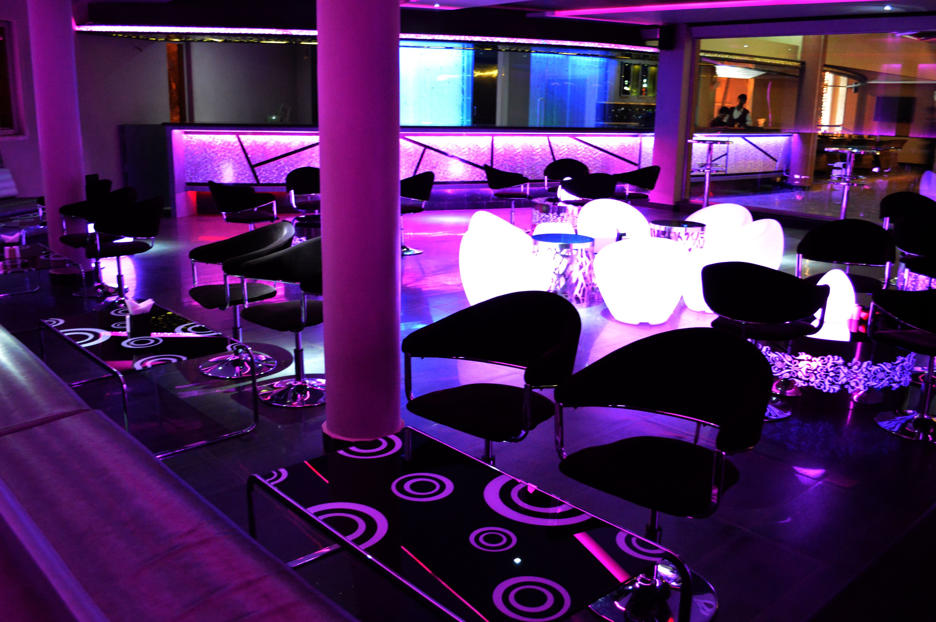 A modern lounge area with black chairs, a bar, and a neon-lit reception desk.