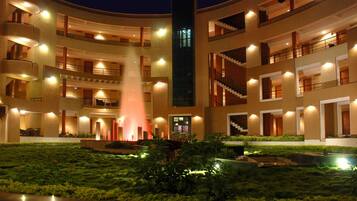 Un hotel de varios pisos con una fuente central, balcones e un patio bien iluminado.