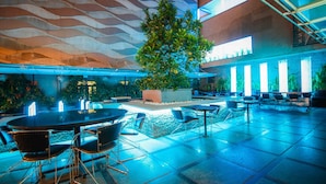 A modern indoor space with a central tree, multiple tables and chairs, and a unique ceiling design. - Hotel Malligi (Hospet)