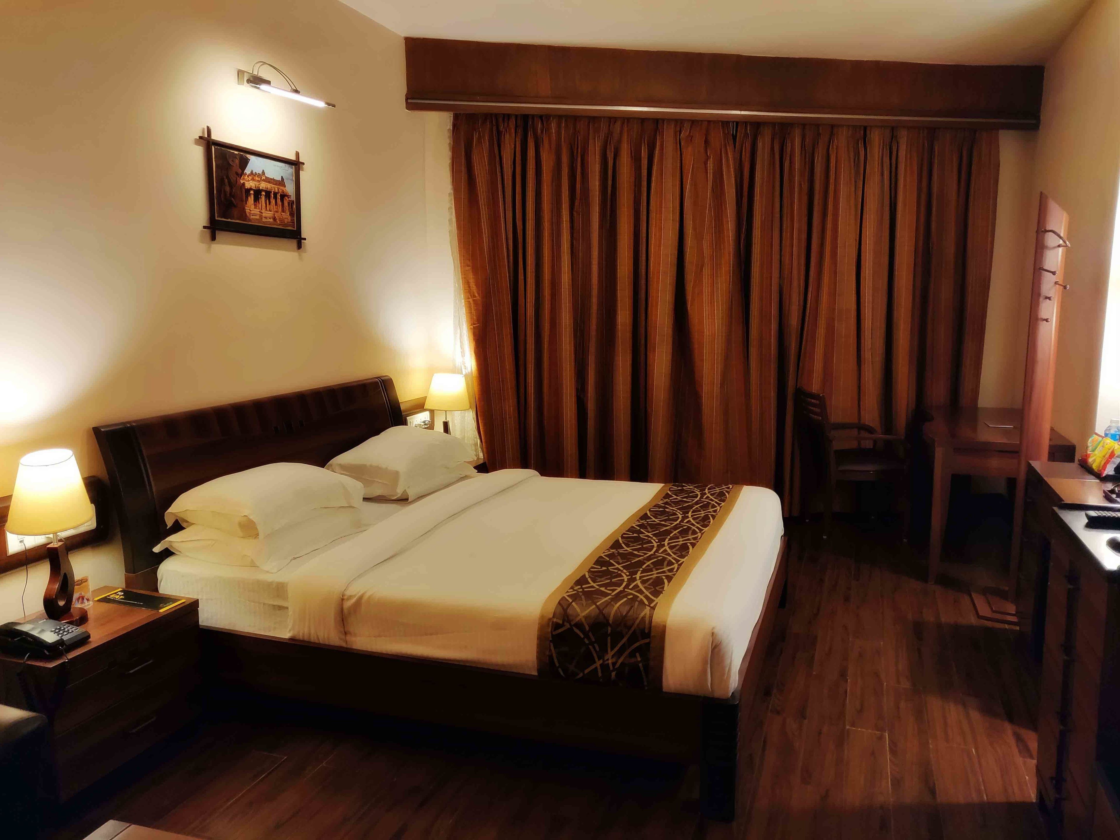 A hotel room with a large bed, two bedside lamps, a desk, and a chair.