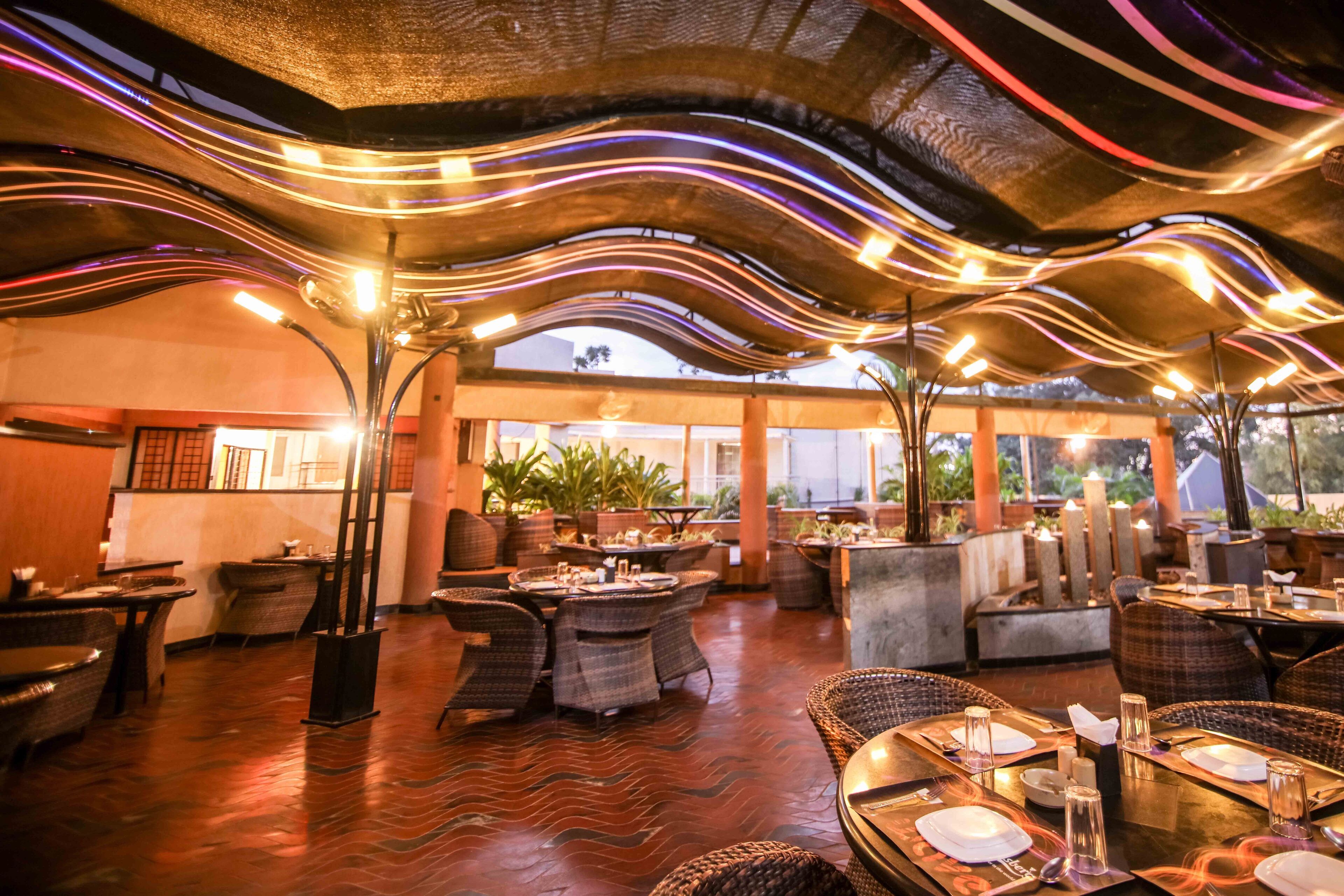 Un espace de restauration intérieur aménagé avec des meubles en osier, des tables dressées et un plafond doté de luminaires.