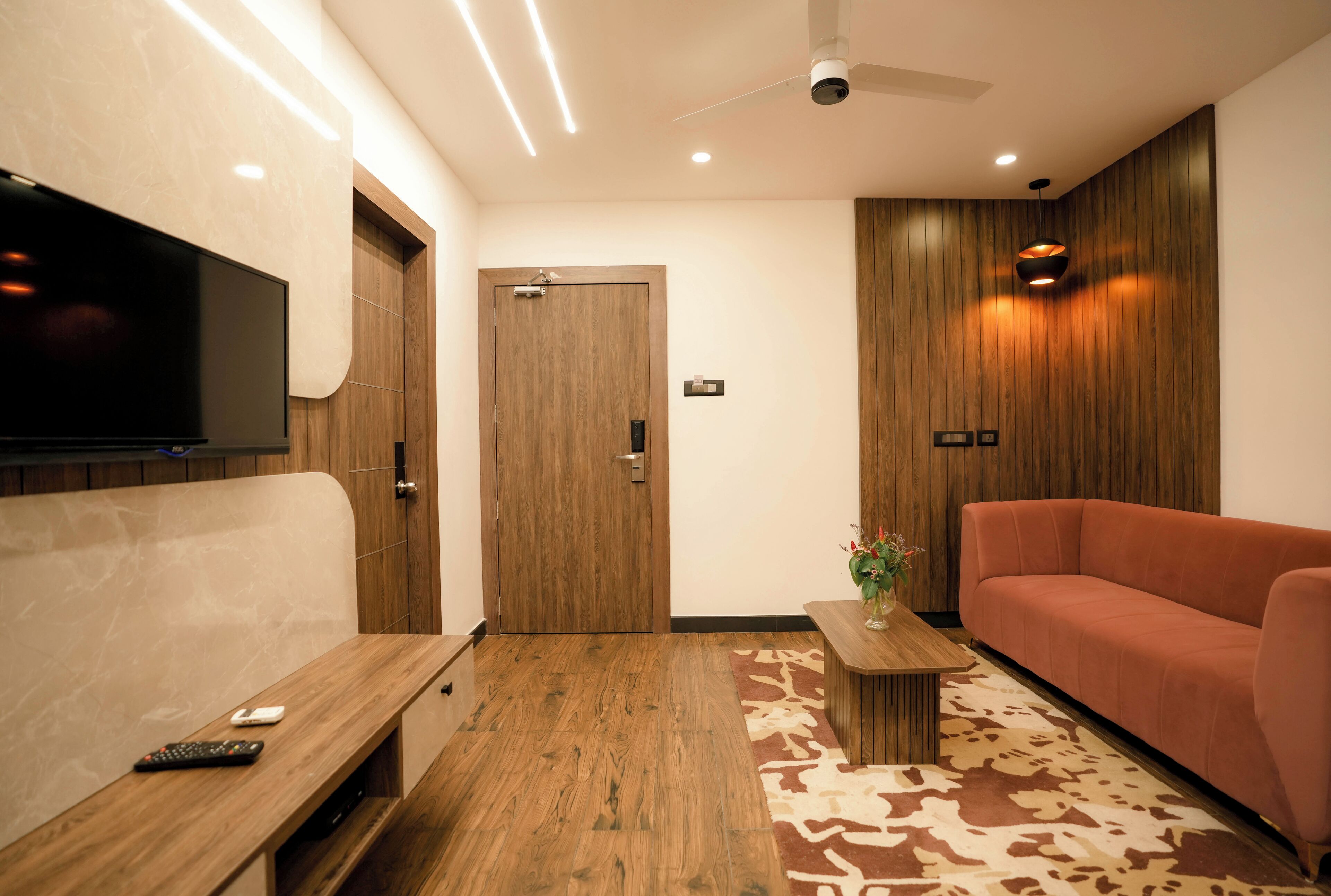 A modern living room with a wooden floor, a sofa, a TV mounted on the wall, and a ceiling fan.