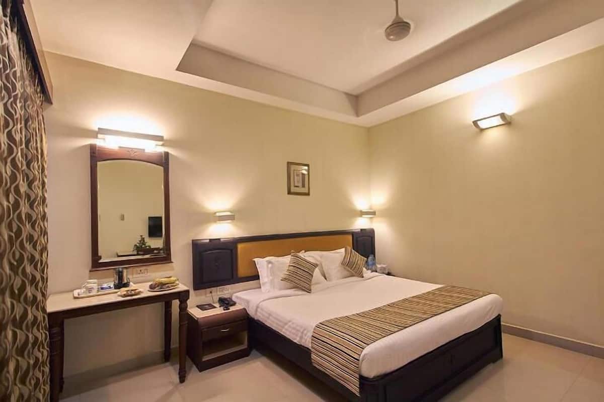 A hotel room with a bed, bedside tables, a mirror, and wall-mounted lights.