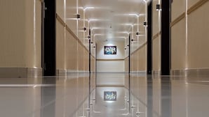 A modern, well-lit hallway with reflective flooring and a central artwork display.