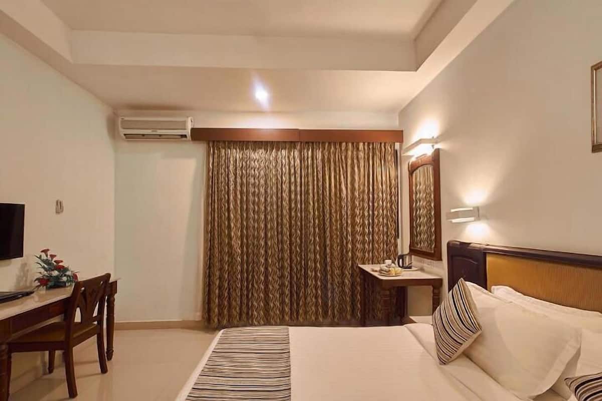 A hotel room with a bed, a desk, a chair, a television, a mirror, and a curtain.