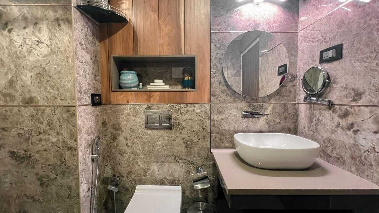 A bathroom with a marble wall, a wooden cabinet, a round mirror, and a white sink.