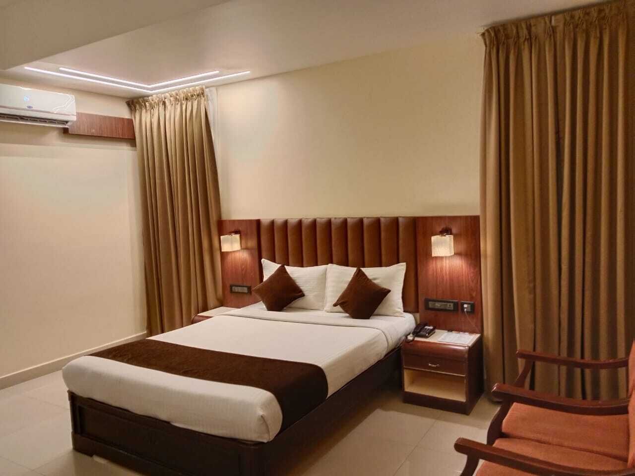 A hotel room with a large bed, two bedside tables, a nightstand, a chair, and a wall-mounted air conditioner.