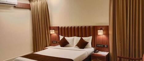 A hotel room with a large bed, two bedside tables, a nightstand, a chair, and a wall-mounted air conditioner.